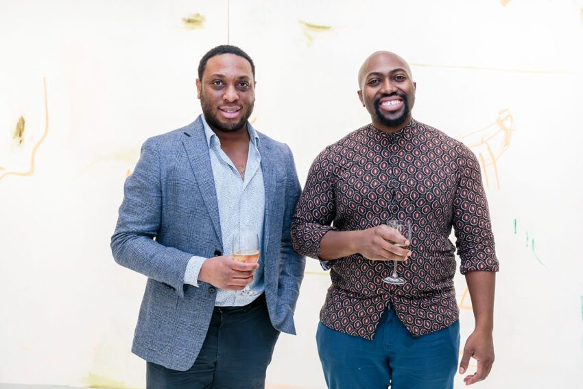Two people smiling and holding glasses in an art gallery with abstract paintings in the background.