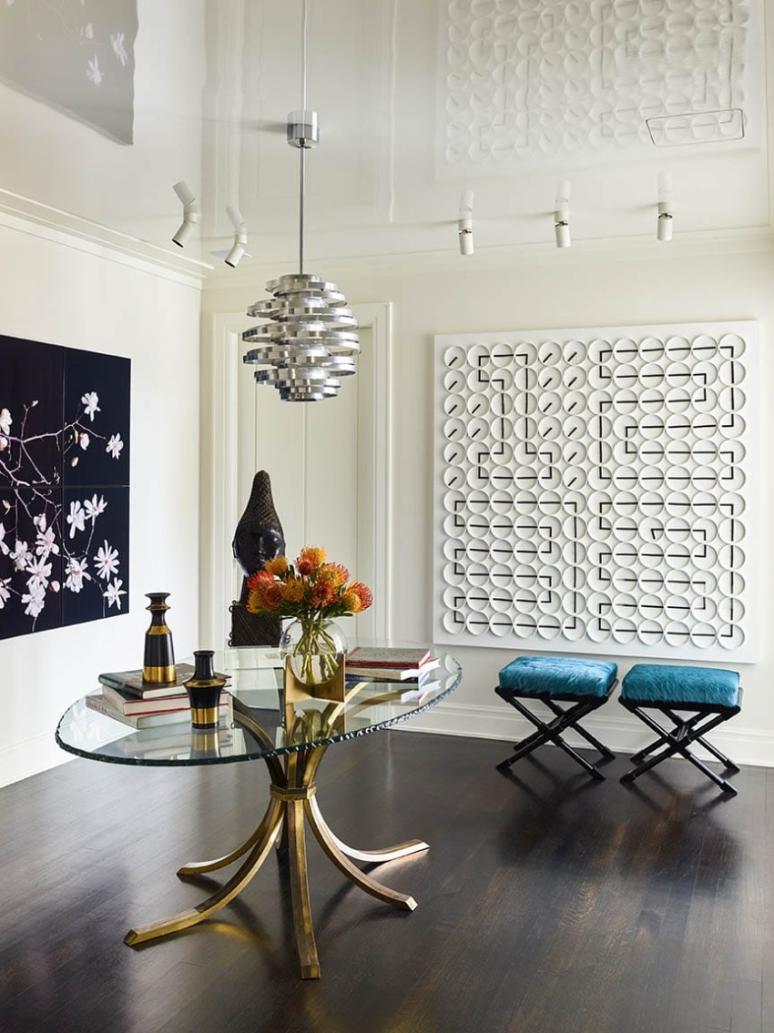 Modern living room with glass table, abstract wall art, pendant light, and floral centerpiece, featuring dark wood floors.