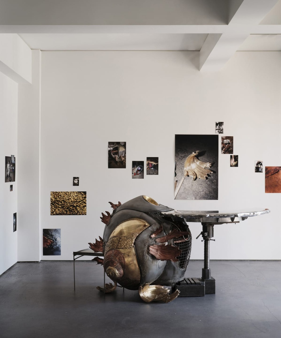 Sculpture of a large, round metallic crab in an art gallery with various photos on the white walls.