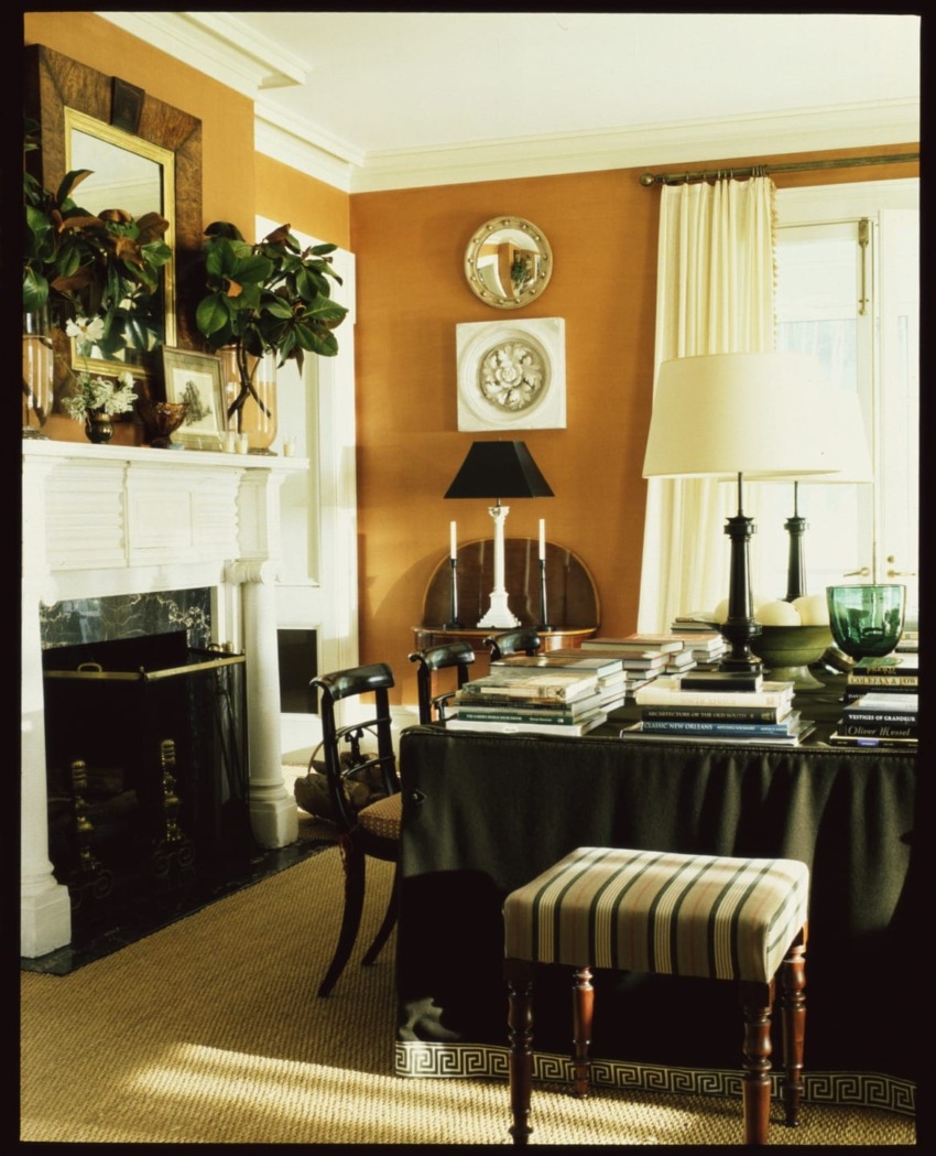Elegant living room with a decorated fireplace, books on a draped table, and a striped stool.