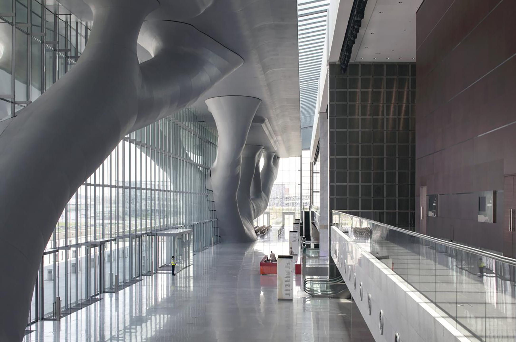 Modern architectural interior with large, curved structures, glass walls, and natural light streaming through windows.