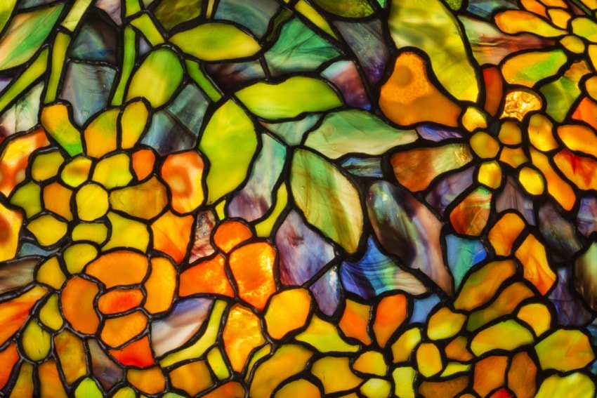 Stained glass window with vibrant floral design in shades of yellow, orange, and green against colorful abstract background