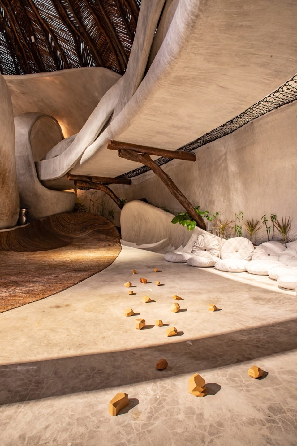 Modern architectural interior with curved walls, natural lighting, and scattered geometric shapes on the floor.