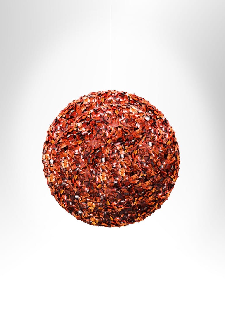 Round pendant light with a textured surface made of red and brown dried leaves against a soft white background.
