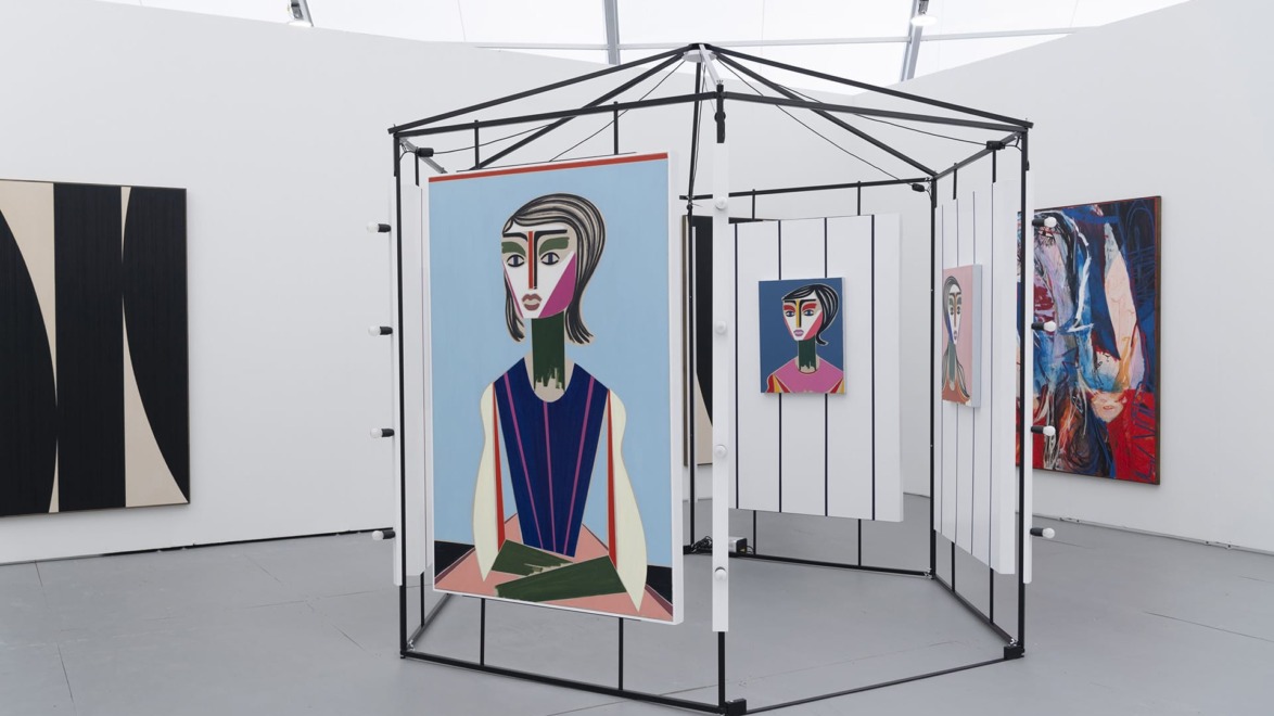 Art gallery display featuring colorful abstract portraits on canvases within a modern geometric installation.
