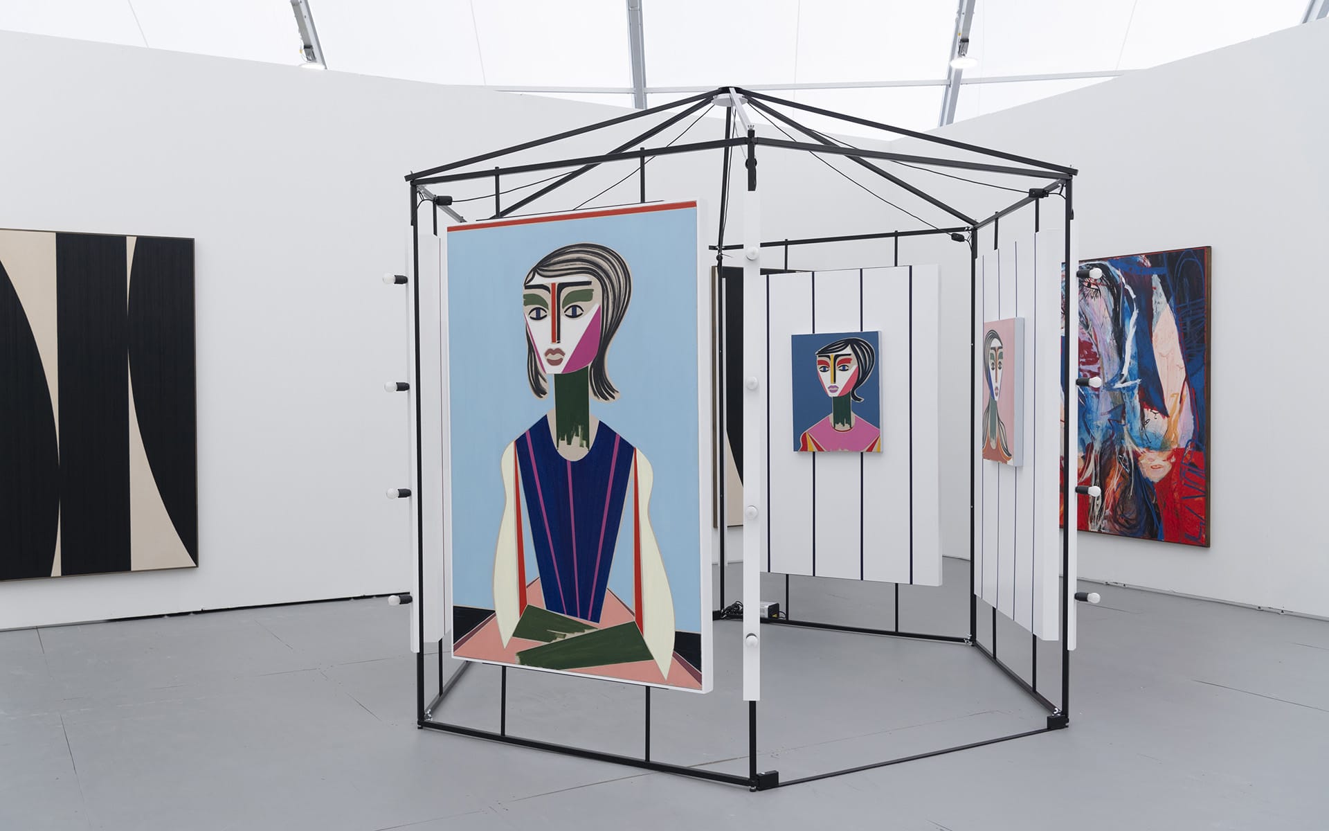 Art gallery display featuring colorful abstract portraits on canvases within a modern geometric installation.