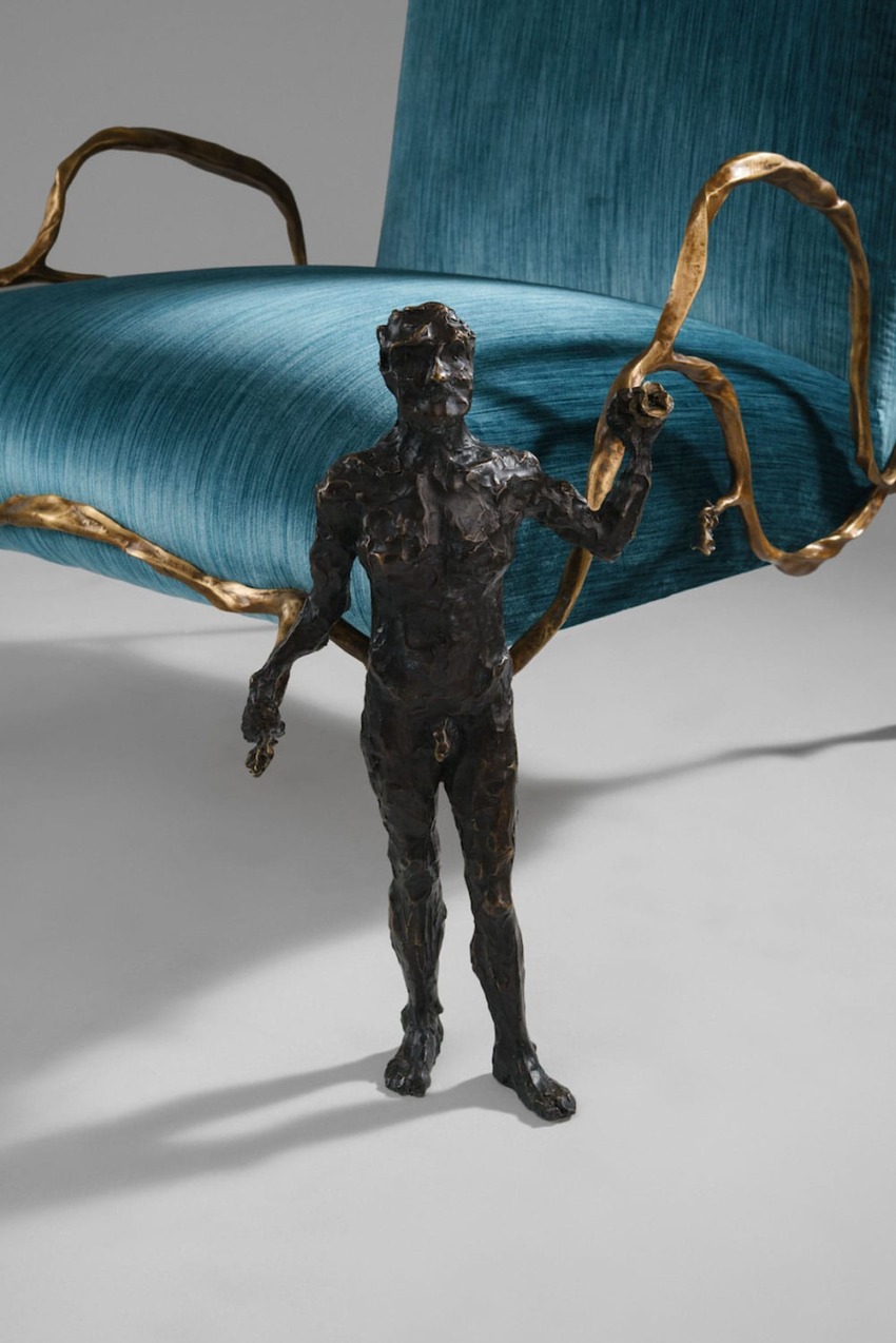 Bronze statue of a small man standing in front of a large blue chair with decorative gold accents.
