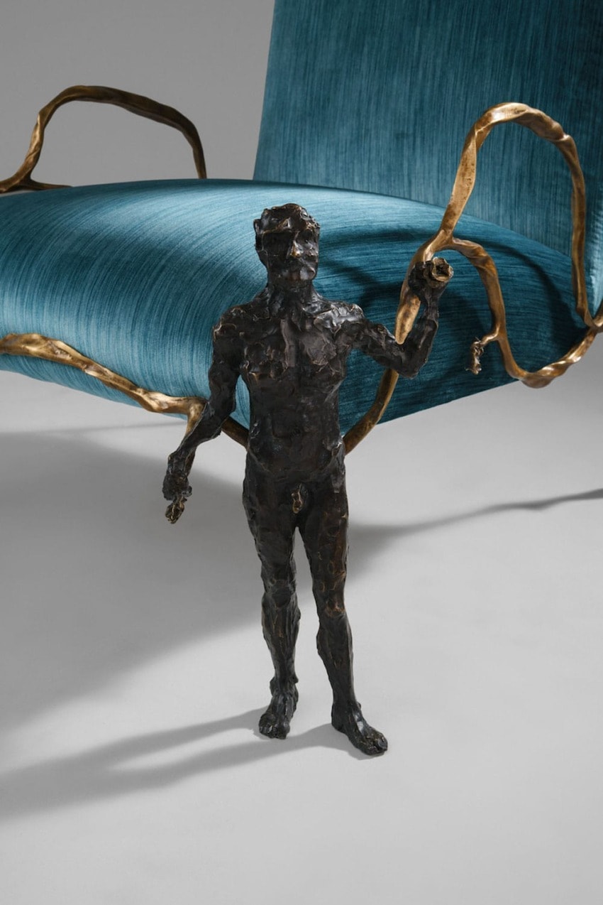 Bronze statue of a small man standing in front of a large blue chair with decorative gold accents.