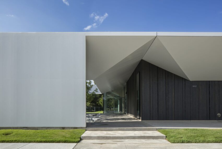 Modern building exterior with geometric design, featuring a white facade and grassy surroundings under a clear blue sky.