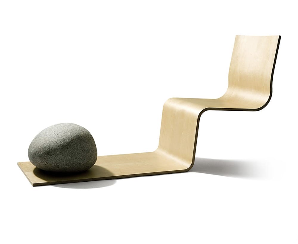 Modern abstract chair design with smooth curves, featuring a large stone placed on the seat against a plain white background.