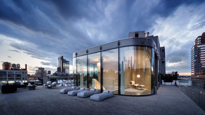 Rooftop patio with modern glass building, city skyline view, and cloud-covered sky at dusk.