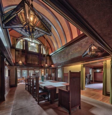 Interior of a classic dining room with wooden furniture, high arched ceiling, and geometric pendant lighting.