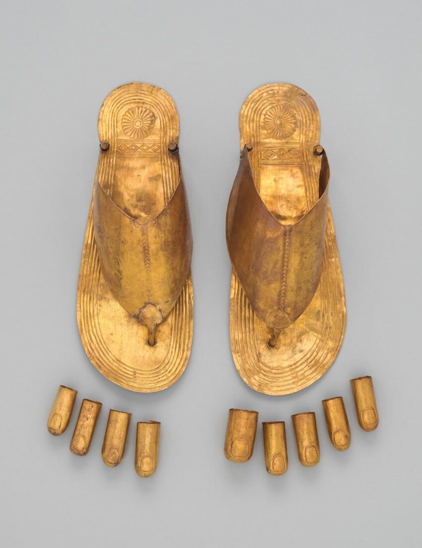 Ancient golden sandals and toe covers displayed on a gray background.