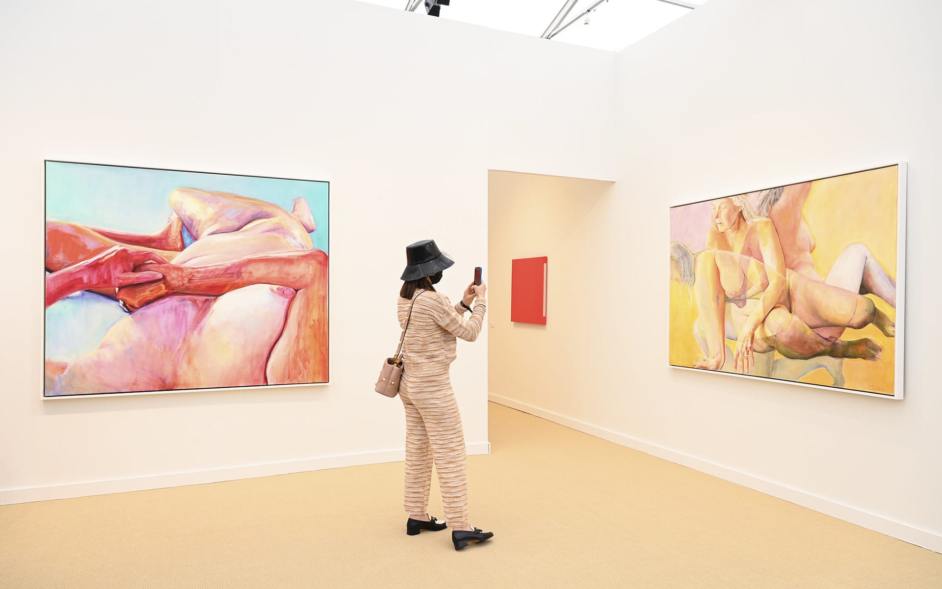 Woman photographing colorful abstract paintings in a gallery with beige walls and carpet.