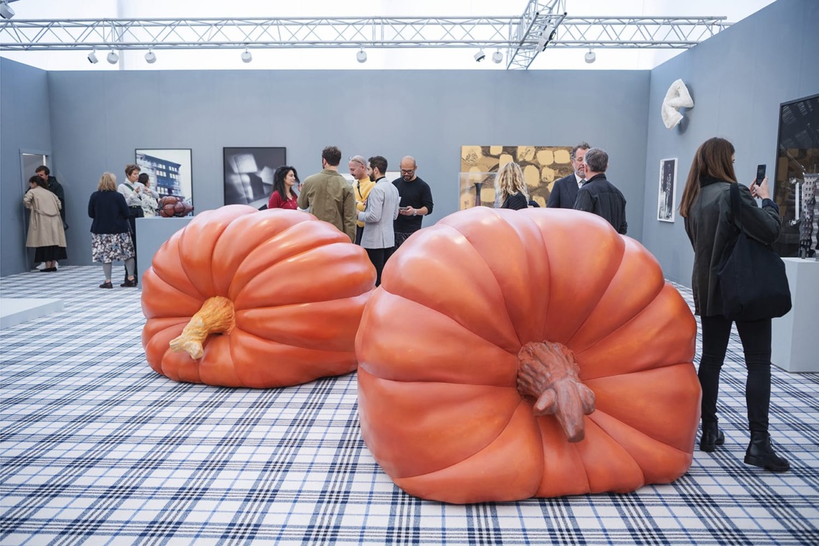 Large pumpkin sculptures in an art gallery setting with people observing the artwork and interacting in the background.