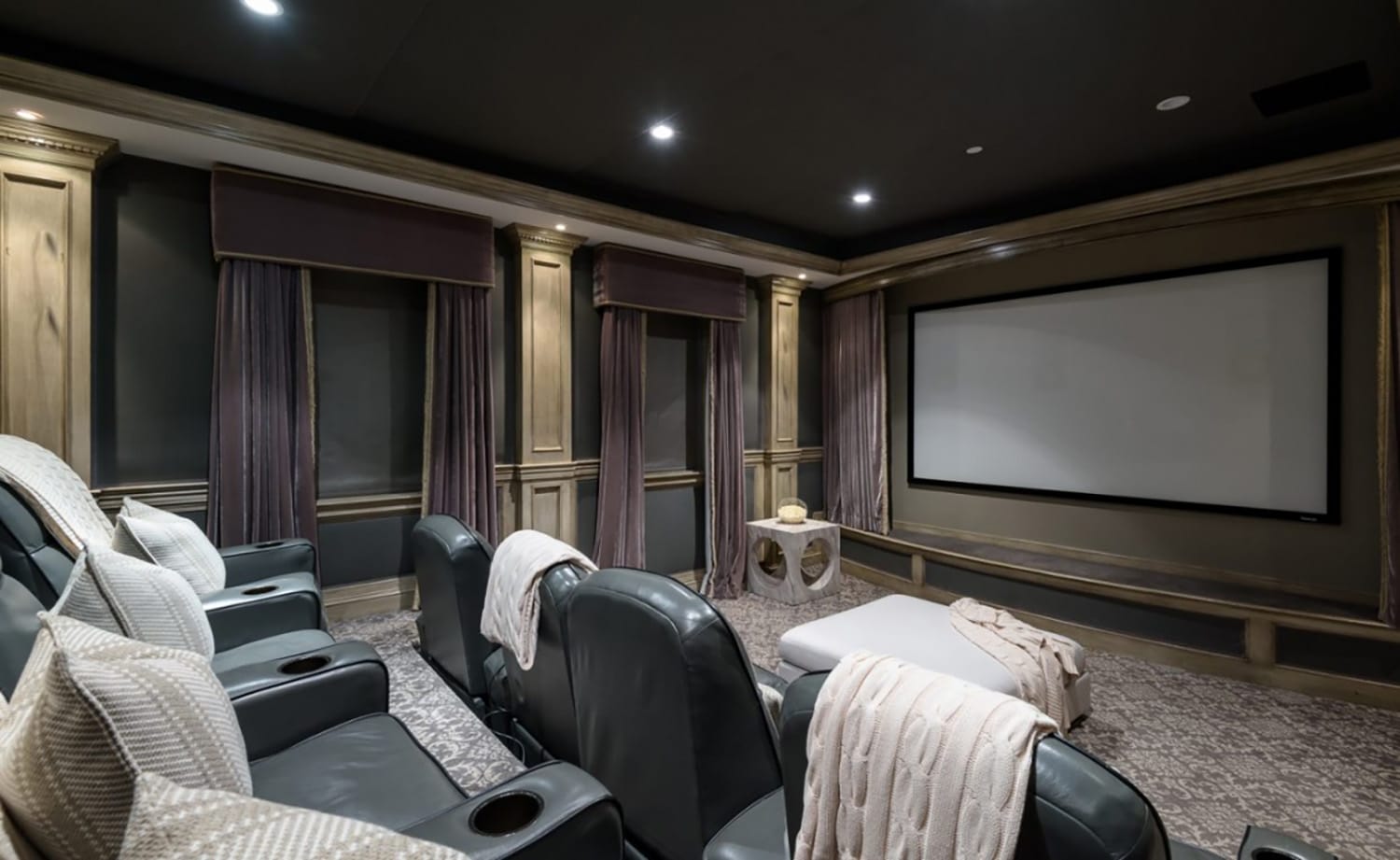 Luxury home theater with plush seating, large screen, and elegant drapes creating a cozy entertainment environment