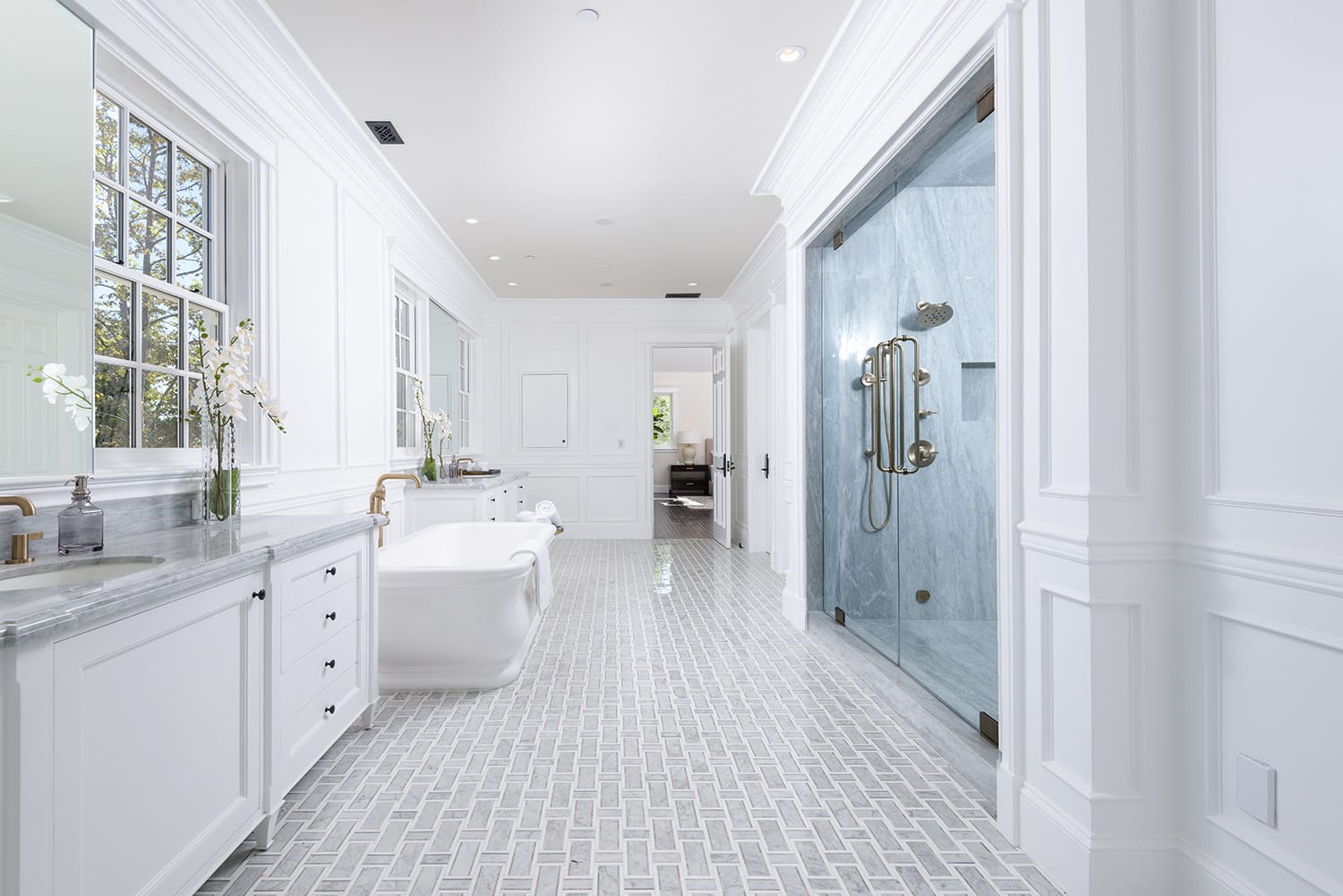 Elegant white bathroom with a freestanding tub, double vanity, glass shower, and large window for natural light.