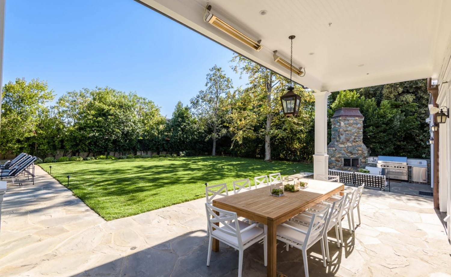 Spacious backyard with patio furniture, green lawn, and outdoor kitchen under clear blue sky.