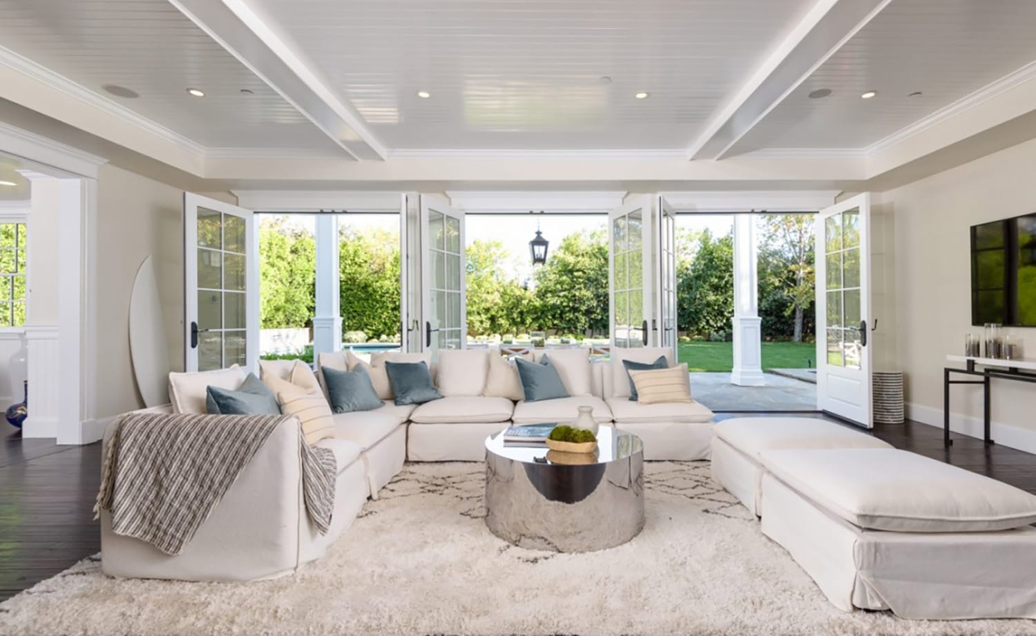 Spacious living room with white sectional sofa, glass doors open to a green garden, and a round metallic coffee table.