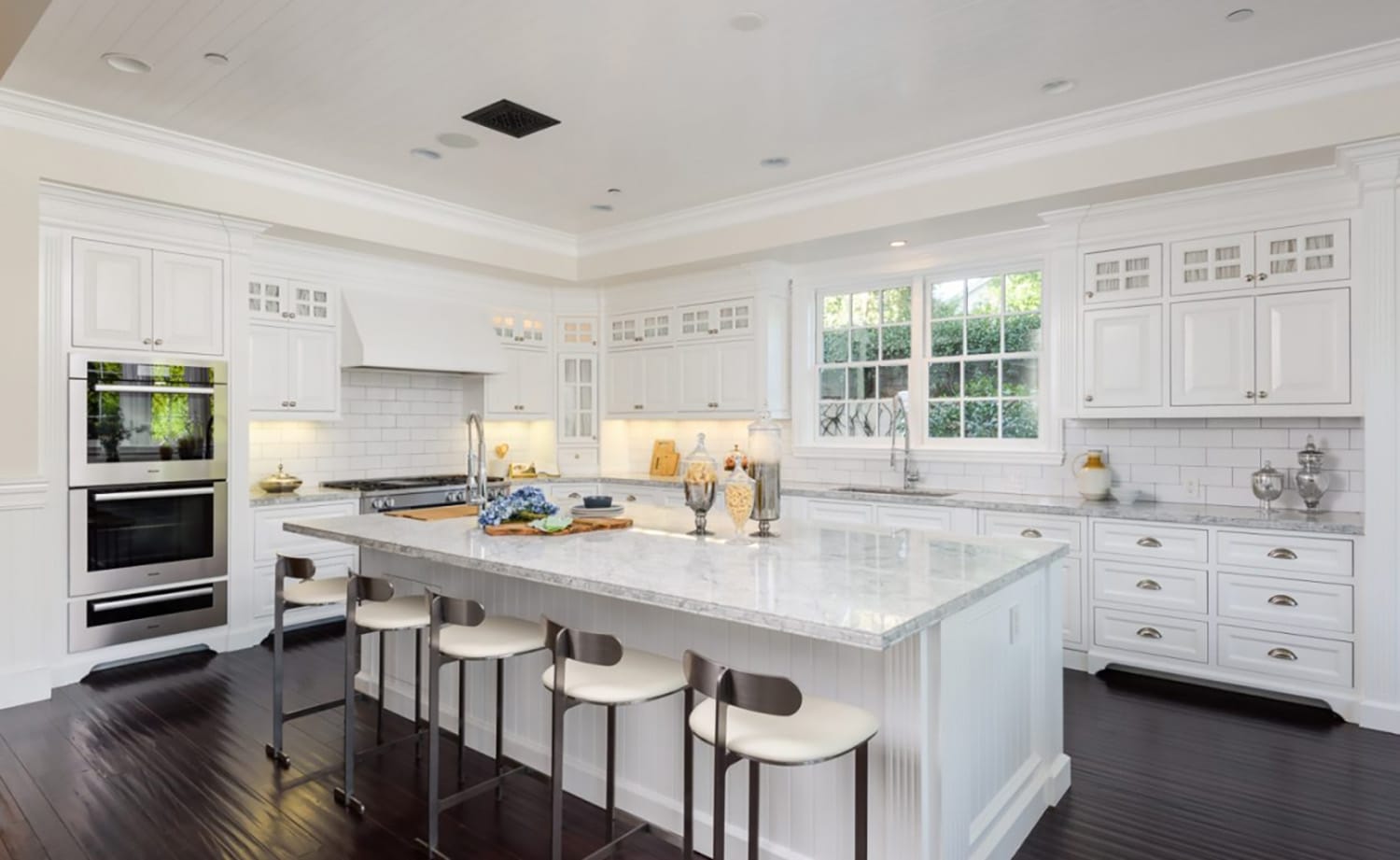 Spacious modern kitchen with white cabinetry, marble island, stainless steel appliances, and dark wood flooring.