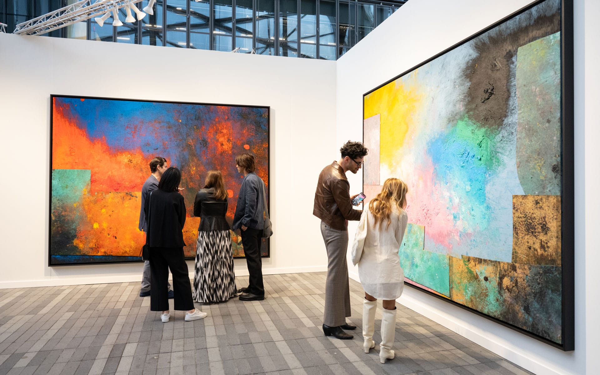 Visitors admiring colorful abstract paintings at an art gallery exhibition with modern architectural surroundings.