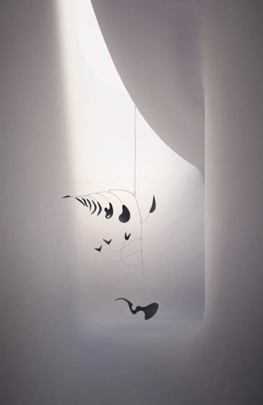 Minimalist mobile sculpture hanging in a soft-lit, curved white space.