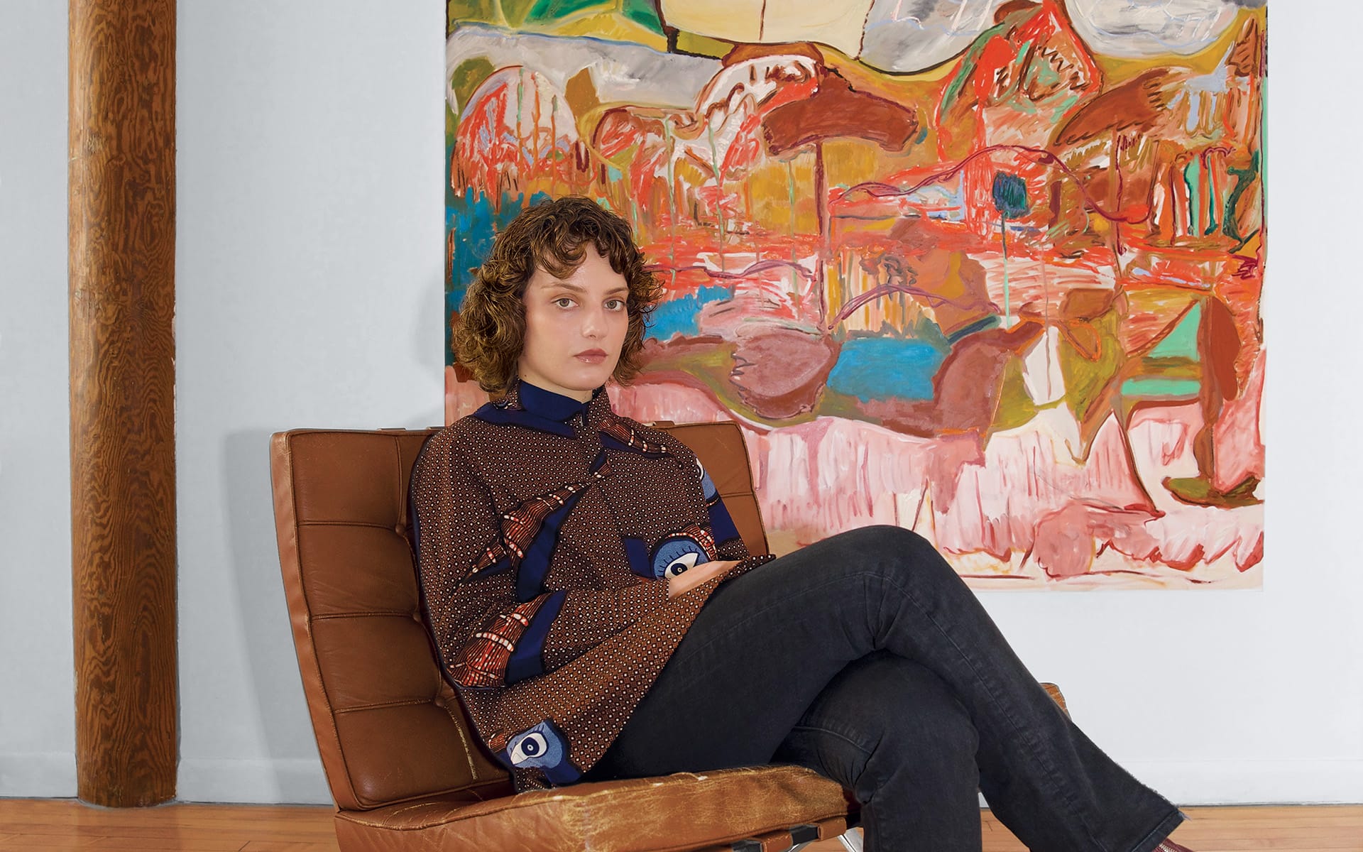 Person sitting on a brown chair with an abstract colorful painting in the background.