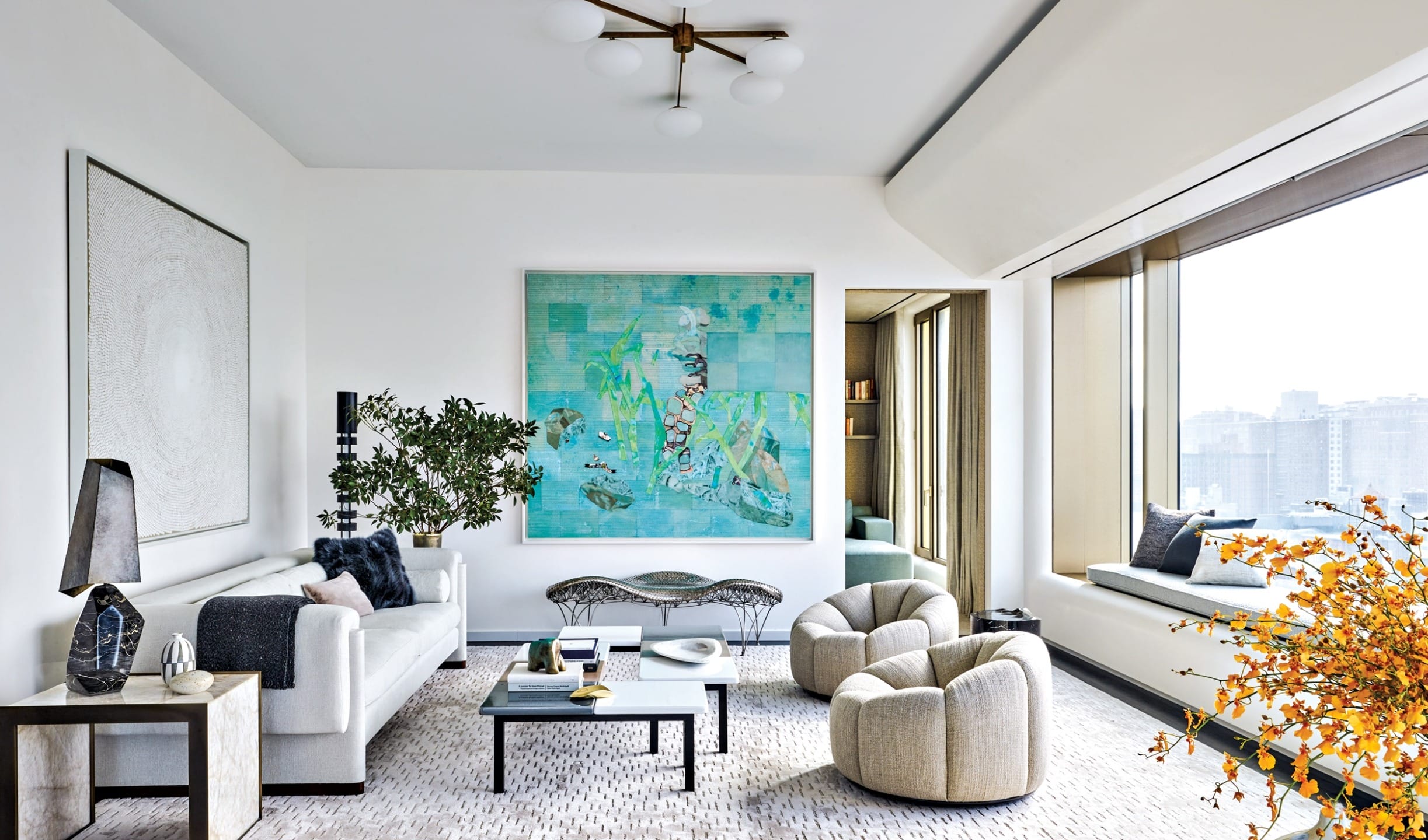 Modern living room with large abstract painting, cozy seating, window nook, and city view.