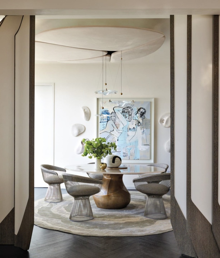 Modern dining room with round table, artistic chairs, green centerpiece, abstract wall art, and circular ceiling feature.