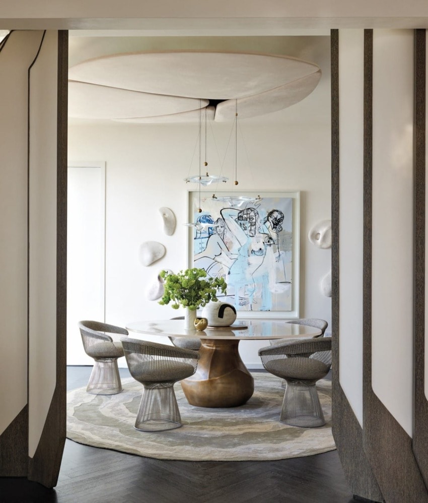 Modern dining room with round table, artistic chairs, green centerpiece, abstract wall art, and circular ceiling feature.