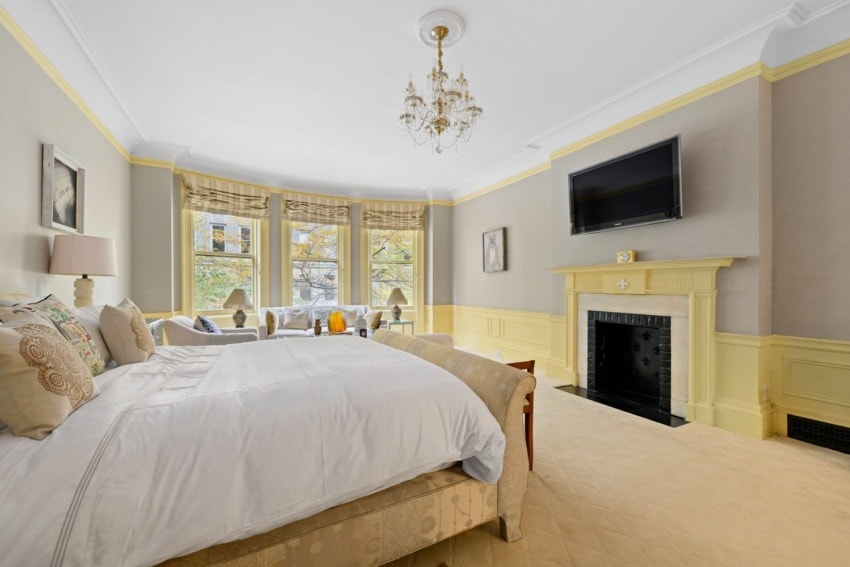 Elegant bedroom with large windows, a fireplace, wall-mounted TV, and a chandelier above a cozy bed.