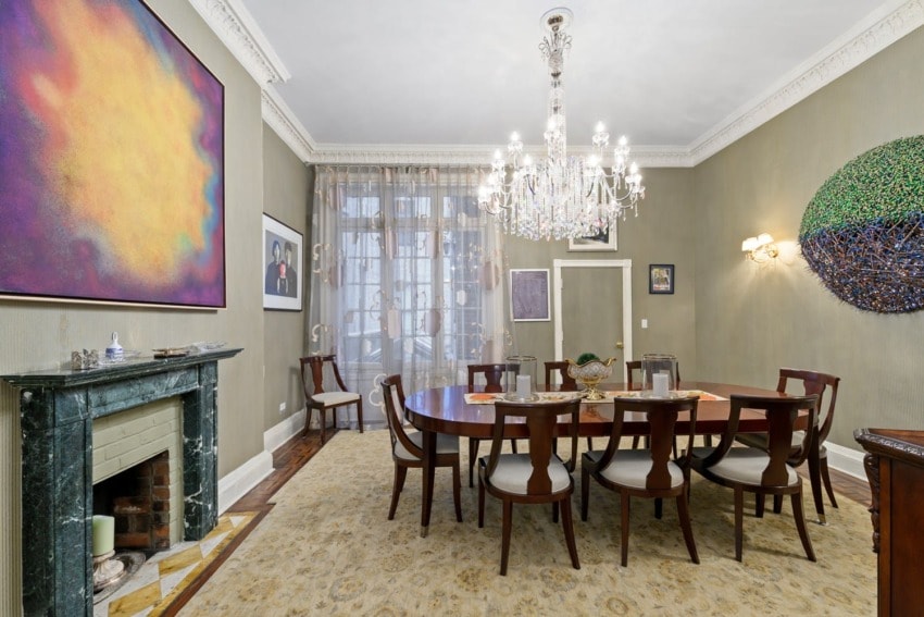 Elegant dining room with a round table, chandelier, fireplace, and colorful abstract artwork on the walls.