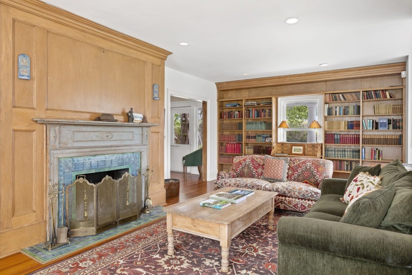 Cozy living room with a fireplace, bookshelves, patterned sofa, green couch, and a wooden coffee table with books.