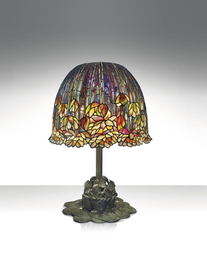 Stained glass table lamp with floral pattern on metal base, set against a plain gradient background.
