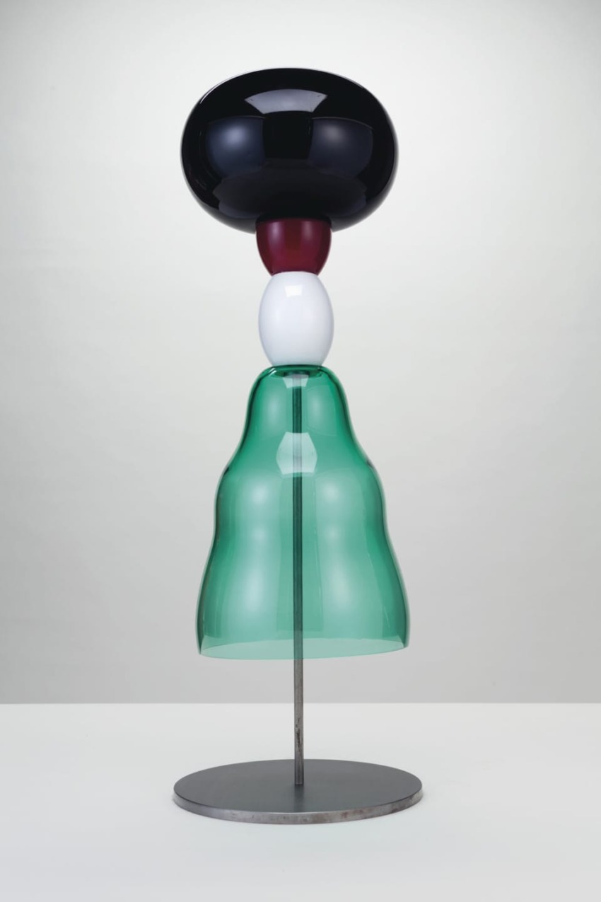Abstract modern sculpture with stacked shapes in black, red, white, and green on a metal base against a light background.