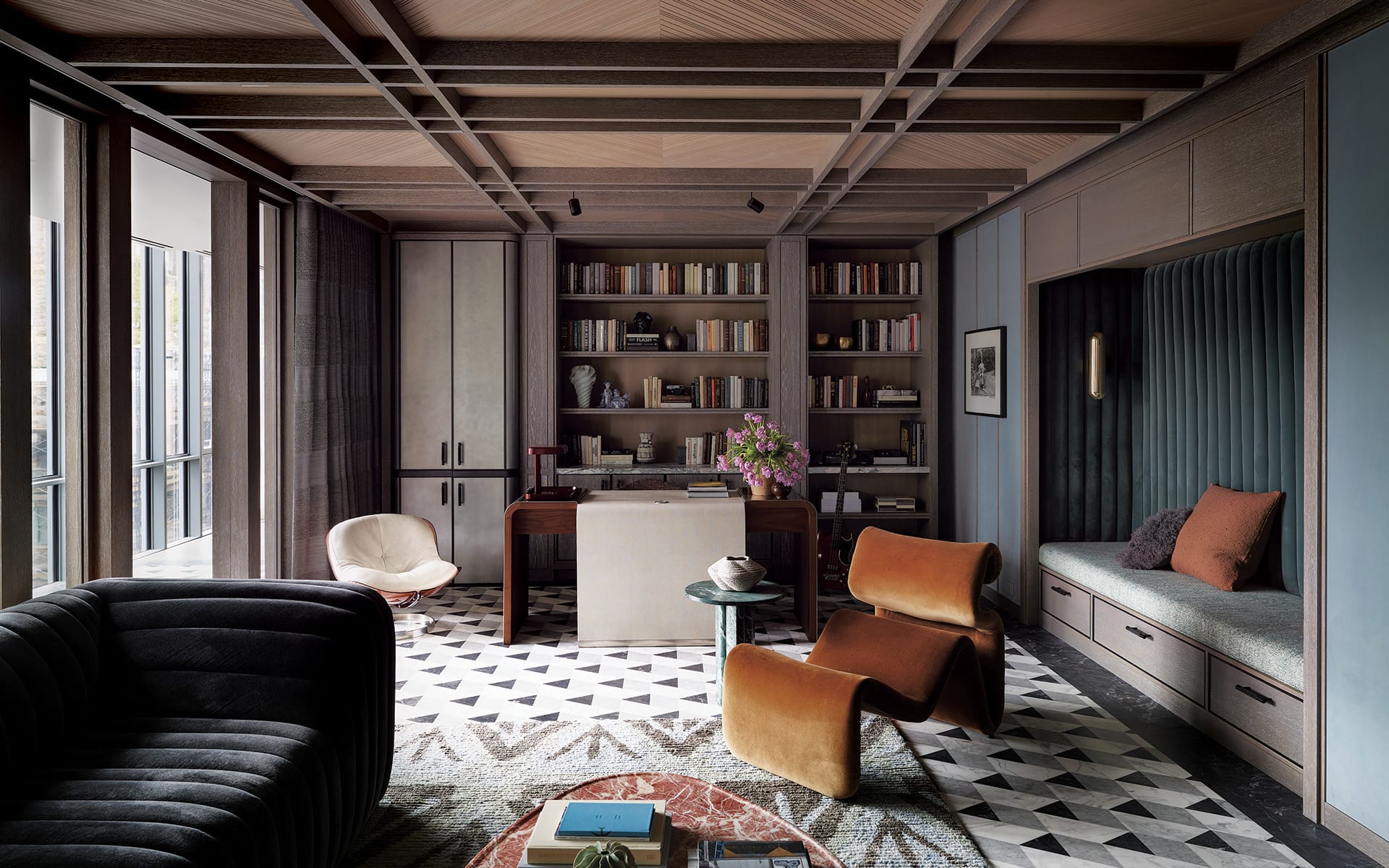 Modern living room with stylish furniture, geometric flooring, built-in bookshelves, and large windows offering natural light.