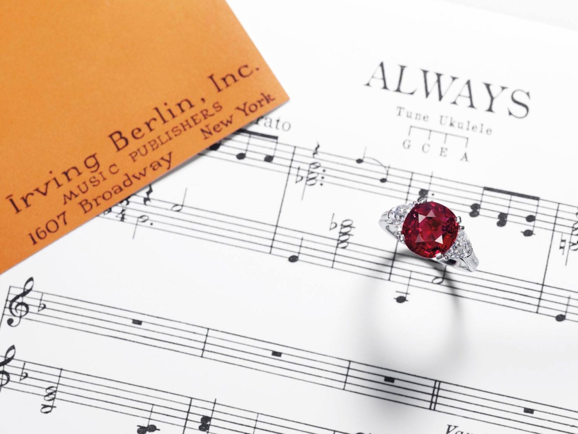 Vintage sheet music with a red gemstone ring placed on top, and an orange Irving Berlin, Inc. music publisher card nearby.