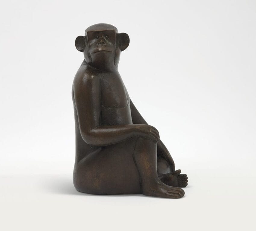 Bronze sculpture of a seated monkey with a contemplative expression against a plain background.