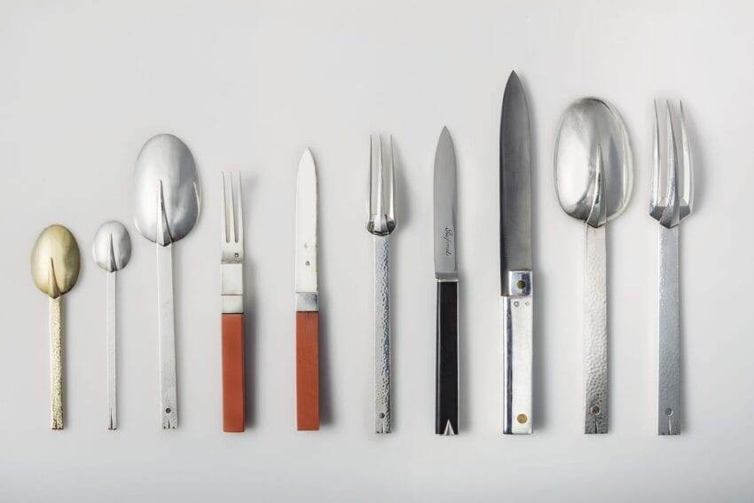 A collection of vintage cutlery with spoons, forks, and knives arranged horizontally on a white background.