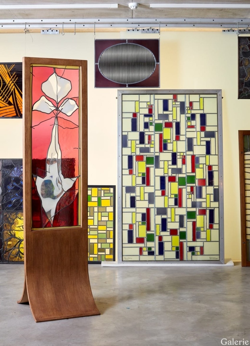 Exhibition of colorful stained glass panels in a gallery setting, featuring abstract geometric and floral designs.