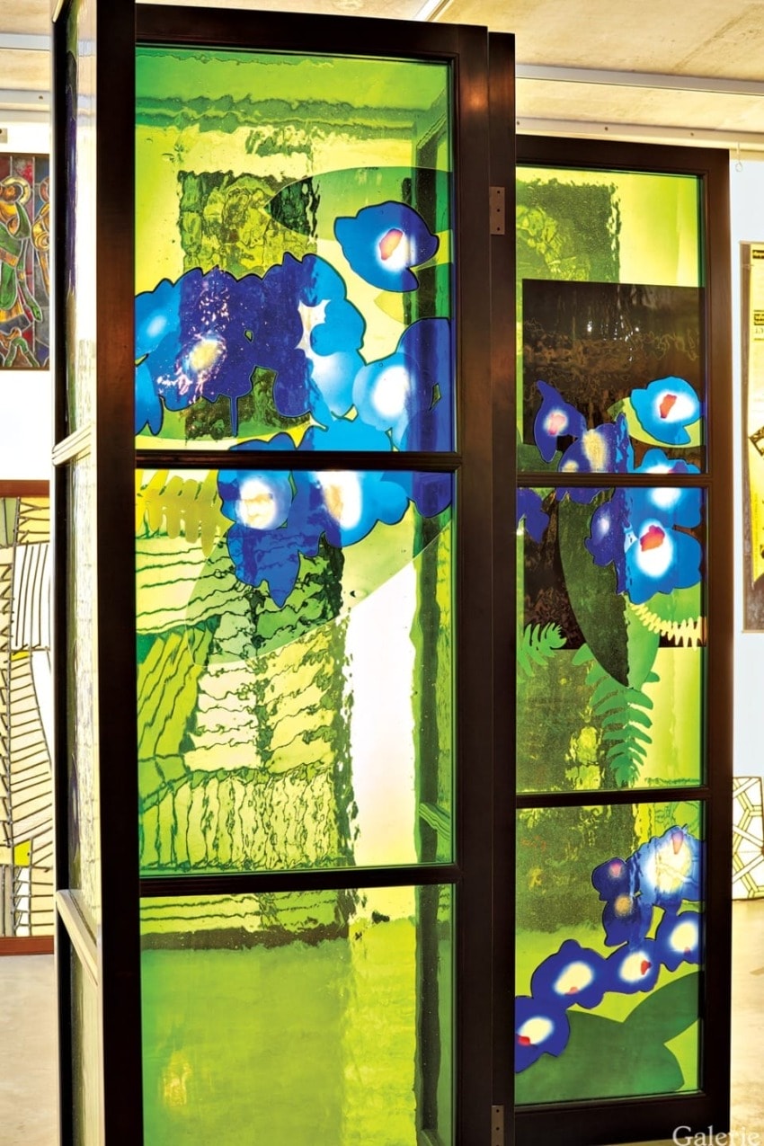 Colorful stained glass panel featuring abstract blue flowers and green foliage in a decorative interior setting.