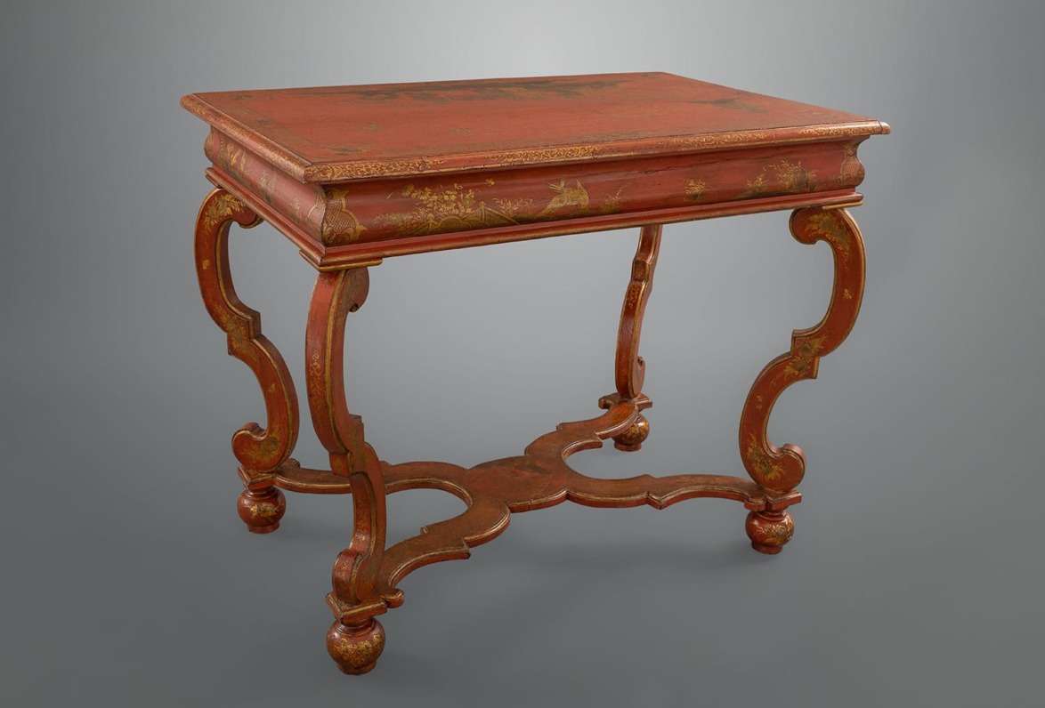 Antique wooden table with intricate carved legs and a reddish-brown finish on a gray background.