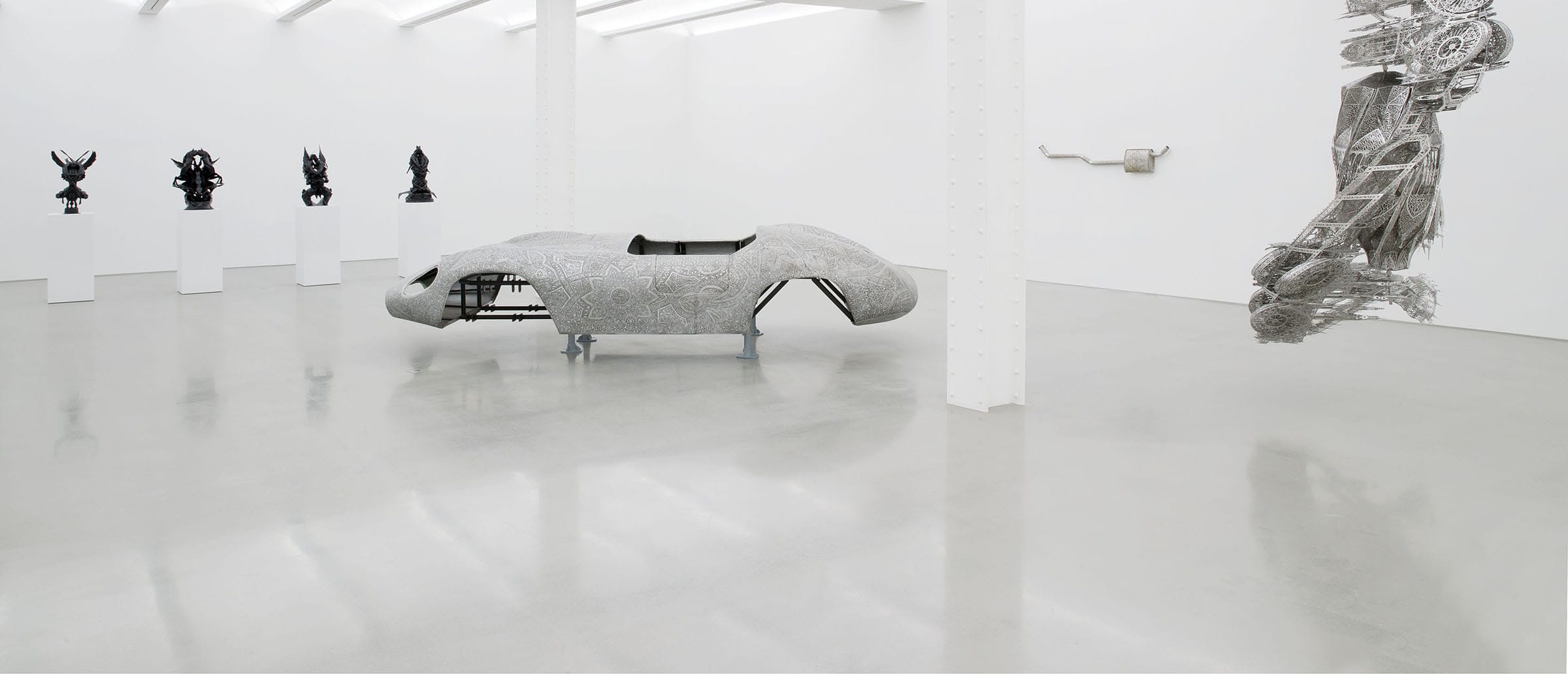 Modern art gallery with abstract sculptures and large, intricate metal centerpiece in a bright, white-walled room.