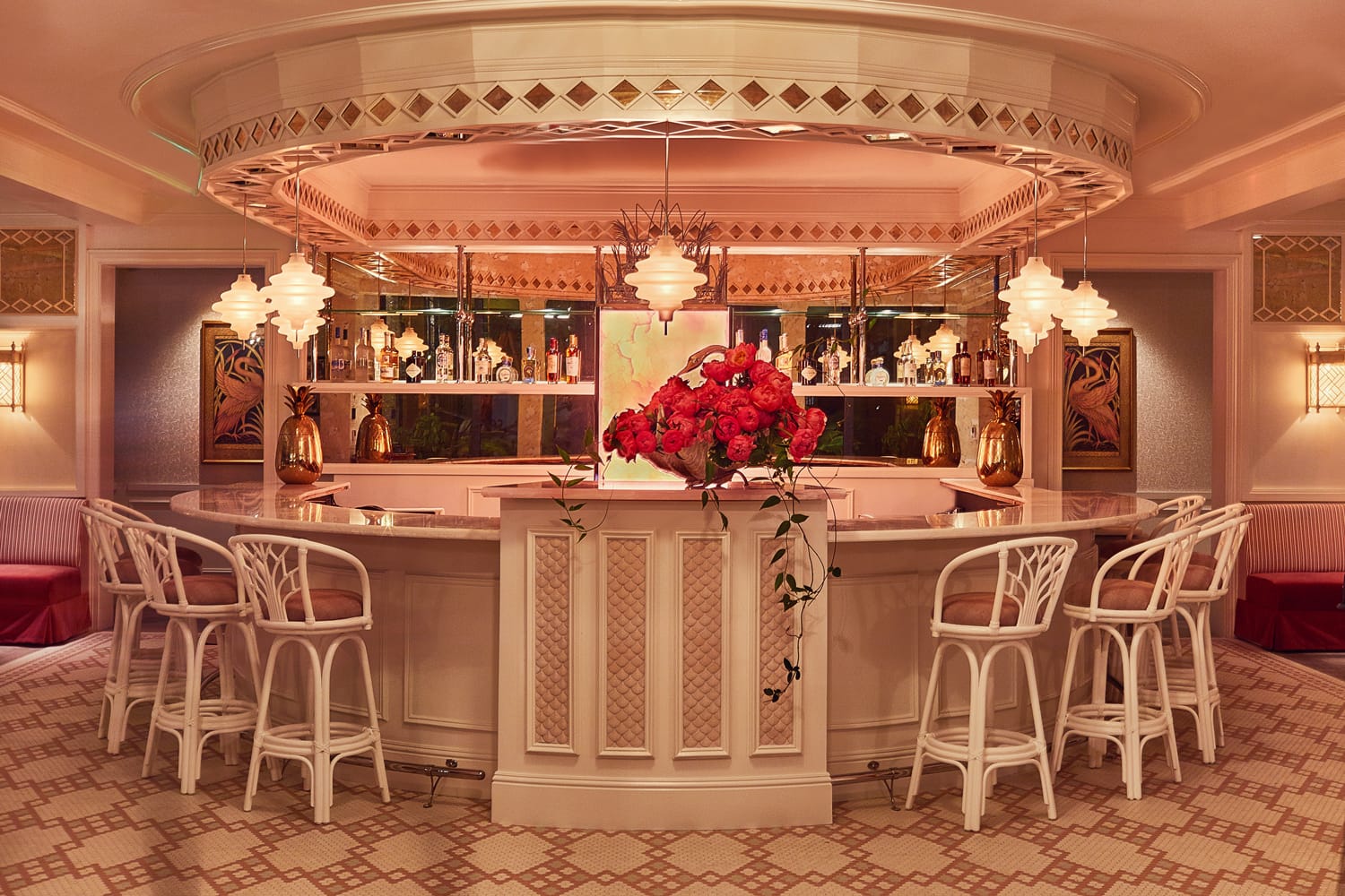 Elegant circular bar with white chairs, vibrant red flowers, and warm lighting, creating a sophisticated and inviting atmosphere.