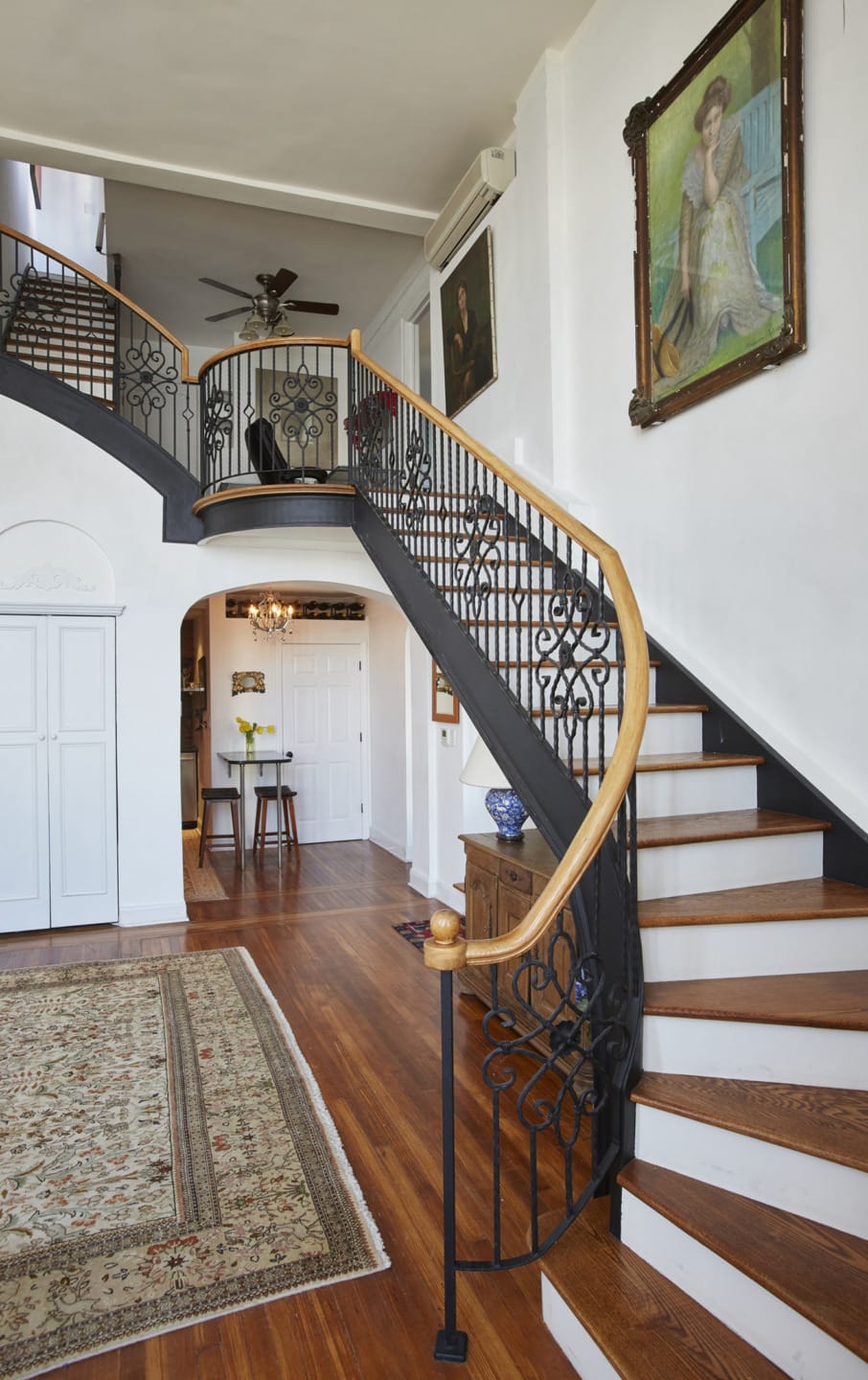 Elegant spiral staircase with ornate black railings, wooden steps, and a decorative rug on the hardwood floor.