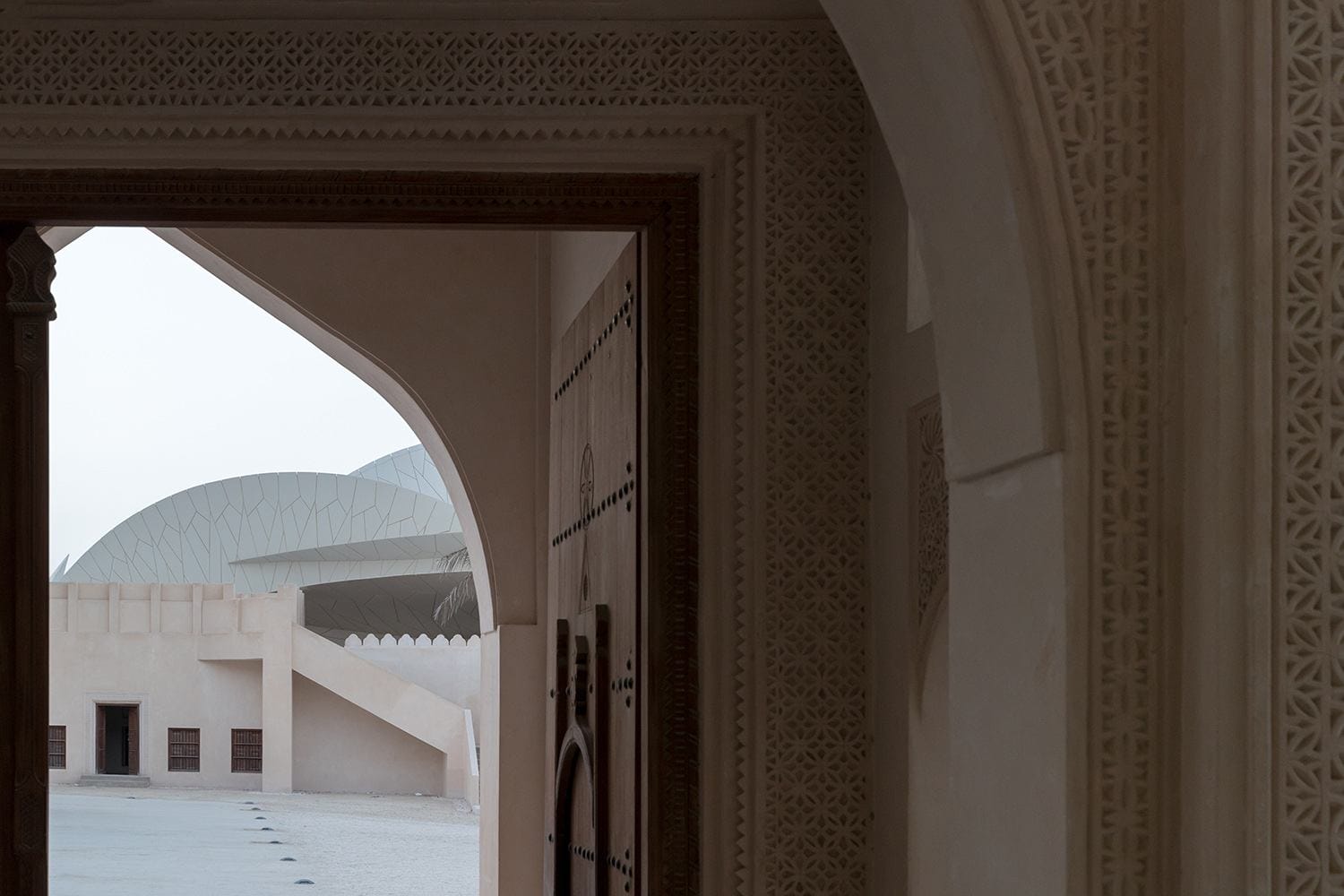 View through ornate doorway to modern architecture with geometric patterns in desert setting.