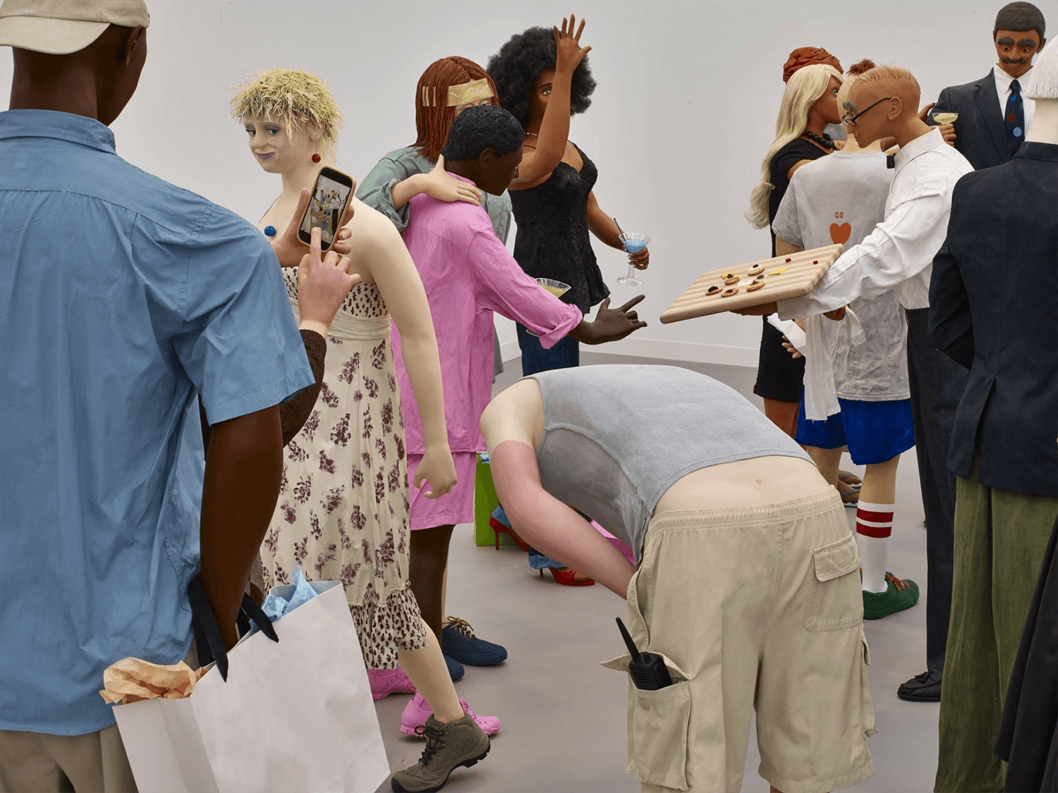 Art installation with realistic sculptures of diverse people interacting at a casual social gathering in a gallery setting.