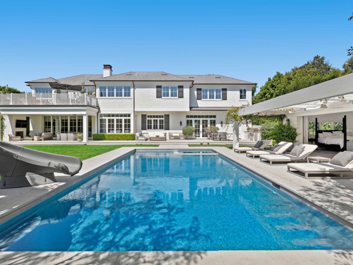 Luxurious backyard with a swimming pool, lounge chairs, and modern white house under a clear blue sky.