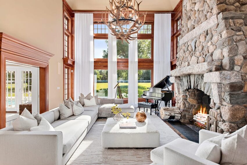 luxurious living room with large windows, stone fireplace, modern furniture, and a grand piano overlooking a scenic lawn