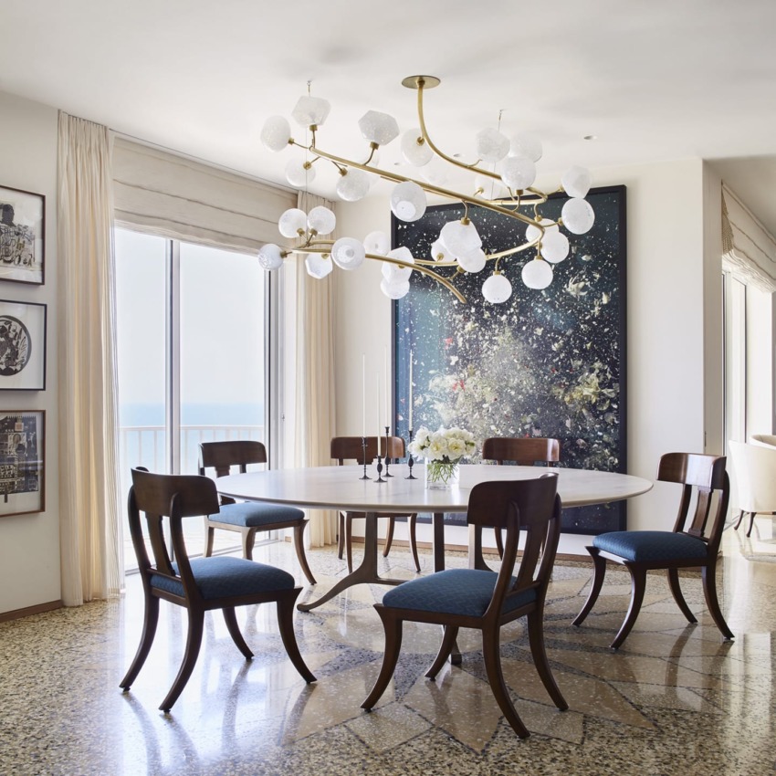 Modern dining room with round table, six chairs, large artistic painting, and unique chandelier above table.